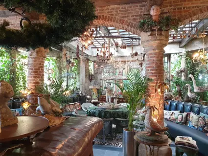 Foto van een serre met gemetselde pilaren en bogen, vol met leren banken, planten en snuisterijen.