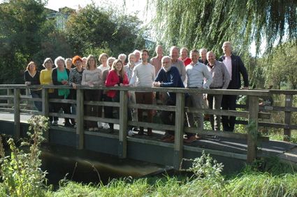 Groepsfoto van mannen en vrouwen op een houten brug met groen en water in de natuur van het Groene Hart.