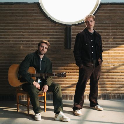 Muziekoptreden van BENR in Het Klooster Woerden, Groene Hart, met het Nederlandse muziekduo poserend voor een bakstenen wand, waarbij een van de muzikanten een akoestische gitaar vasthoudt.