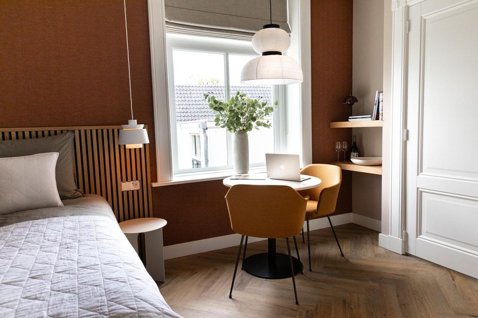 Moderne hotelkamer van Boutique Pastorale in Montfoort met comfortabel bed, ronde tafel met stoelen, werkplek bij het raam en warm interieur in aardetinten.