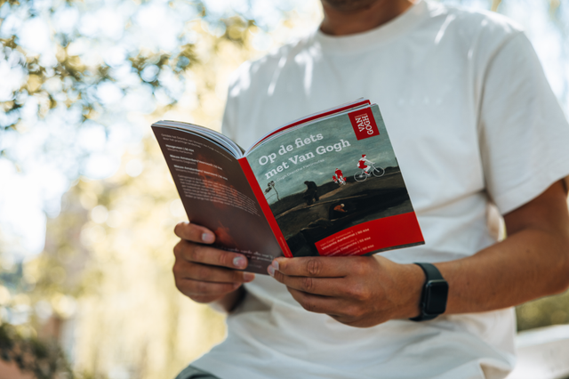 Een man leest in het fietsrouteboekje 'Op de fiets met Van Gogh'.