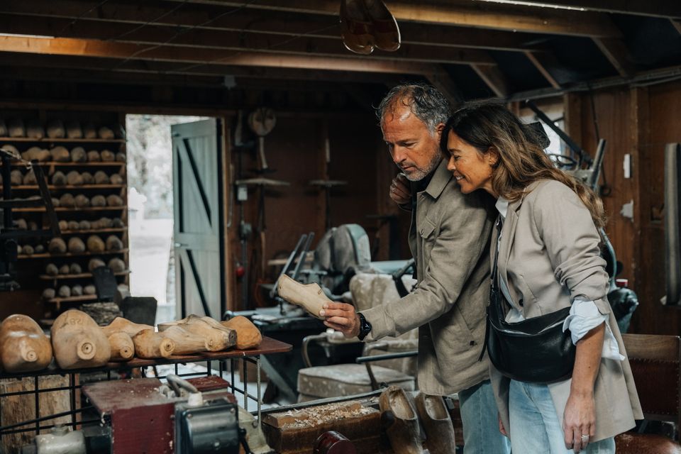 Een man en een vrouw bekijken de mallen van de klompen in de klompmakerij.