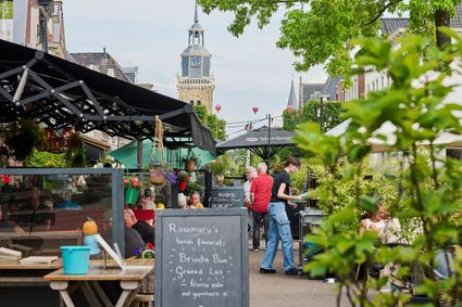 Meerdere restaurants aan de Midstraat in Joure, met de luifel uit en mensen zittend op het terras. Op de achtergrond staat de kerktoren.