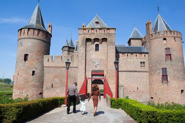 Twee volwassenen lopen met kindje tussen hen in de brug naar het Muiderslot op