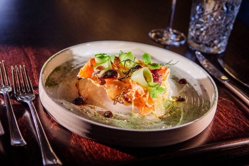 Stijlvol gerecht bij restaurant De Heeren van Montfoort met zalm, frisse groentelinten, kruiden en verfijnde saus, geserveerd op een licht bord op een gedekte tafel.