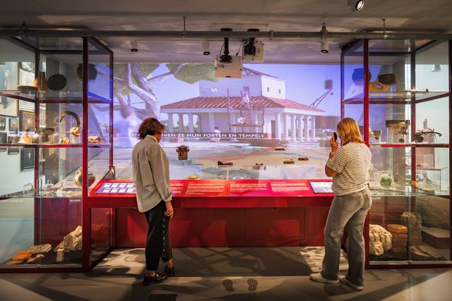 Twee bezoekers bij een afbeeldig van een Romeinse tempel