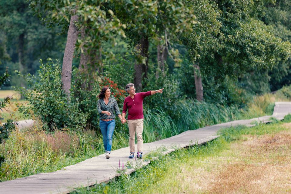 Een man en vrouw wandelen over een houten vlonderpad door een natuurgebied in Drenthe.
