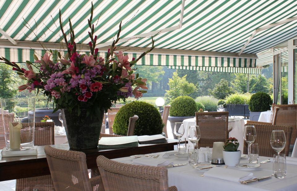 Terras onder groen-witte luifel met ingedekte tafels en een groot bloemstuk.