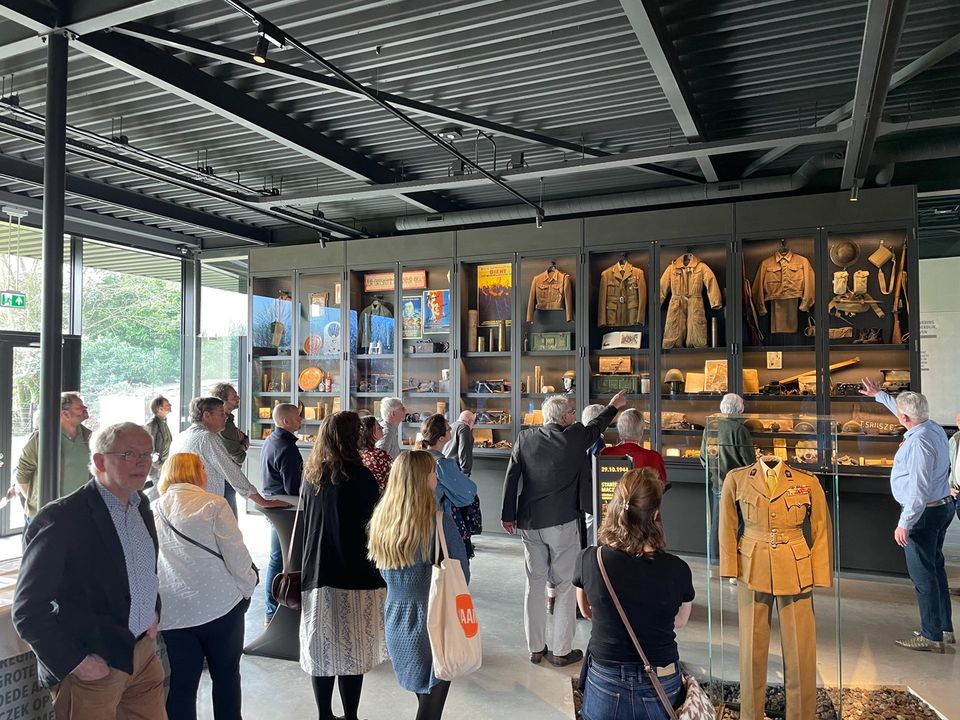 Groep mensen bekijkt vitrinekast met allerlei voorwerpen uit de Tweede Wereldoorlog.