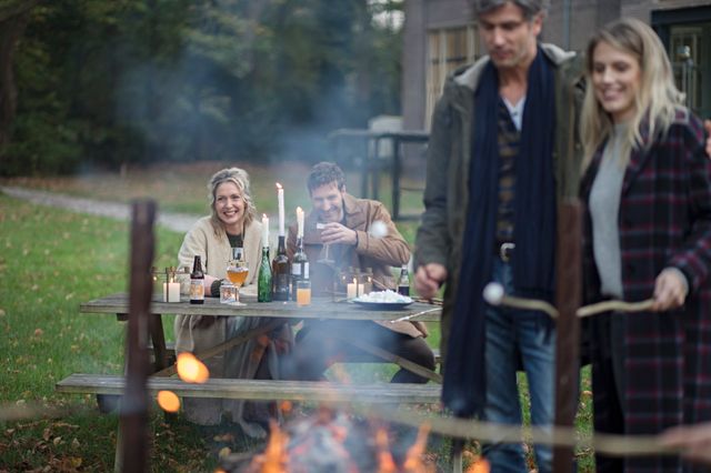 Twee stellen zitten met een drankje bij het kampvuur en roosteren marshmallows.