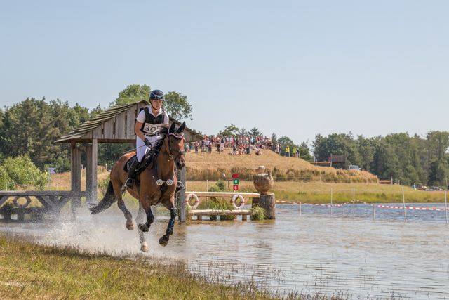 Een meisje galoppeert met een paard langs het water tijdens de discipline eventing van paardrijden in Flevoland