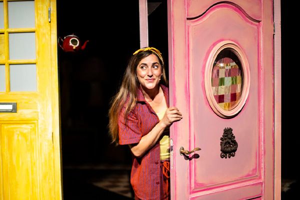 Theatervoorstelling Het Muizenhuis: Sam & Julia op avontuur in Het Klooster in Woerden, Groene Hart, kleurrijk decor met een actrice die nieuwsgierig door een roze deur kijkt tijdens een familievoorstelling voor kinderen.