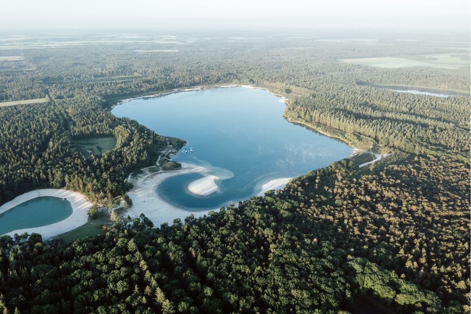 Dronefoto van een uitgestrekt bos met twee helder blauwe zwemplassen met witte stranden.