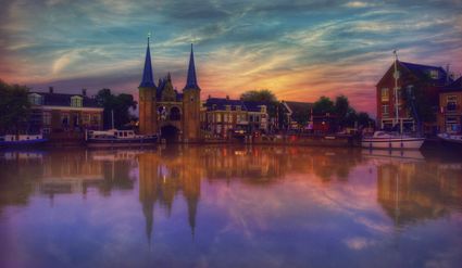 Foto van de Waterpoort in Sneek bij avondlicht, de lucht kleurt blauw, geel en roze, het water paars.