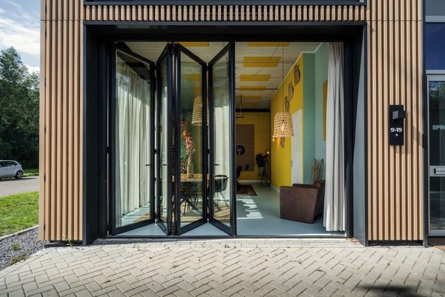 Een foto van de voorgevel met de deuren geopend, je kunt de gekleurde ruimte deels inkijken.