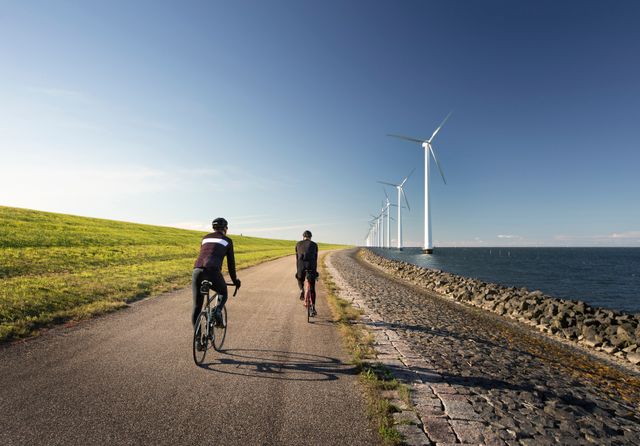 Fietsers op de IJsselmeerdijk met aan de ene kant water en windmolens en aan de andere kant de dijk in Flevoland
