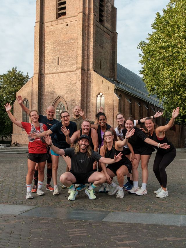 Kerkplein met stadskerk in Woerden, Groene Hart, groepsfoto van deelnemers aan een social run van de Offline Outside Social Club die na het hardlopen poseren op het plein voor de monumentale bakstenen kerk.