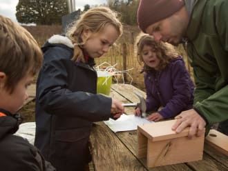 Kinderen timmeren een vogelhuisje met hulp van de boswachter