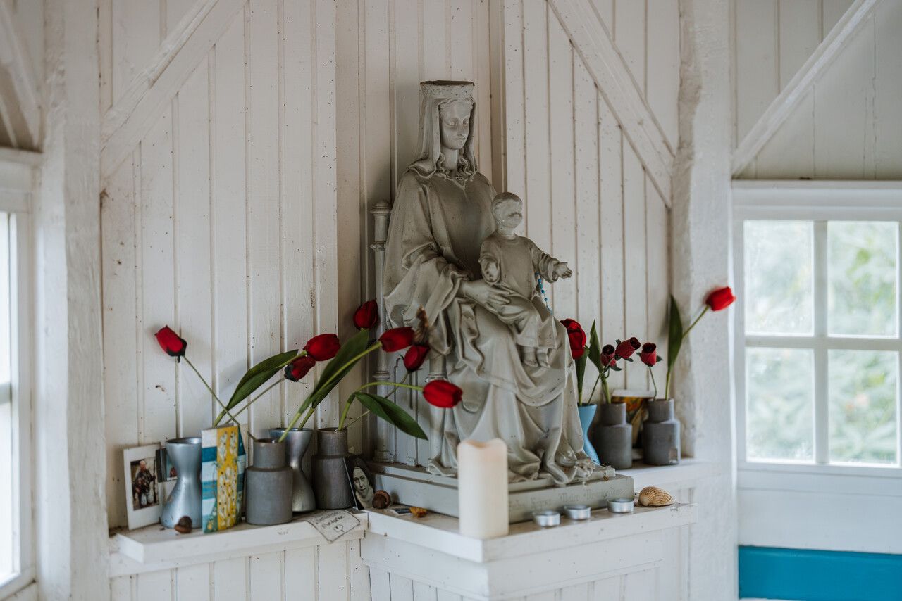 Interieur kapel, mariabeeld omringd door vaasjes met tulpen en kaarsjes.