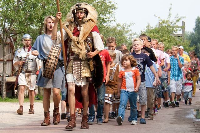 Romeinse soldaat in ceremoniële uitrusting leidt een groep kinderen en ouders door Archeon tijdens een interactieve rondleiding in het Groene Hart.