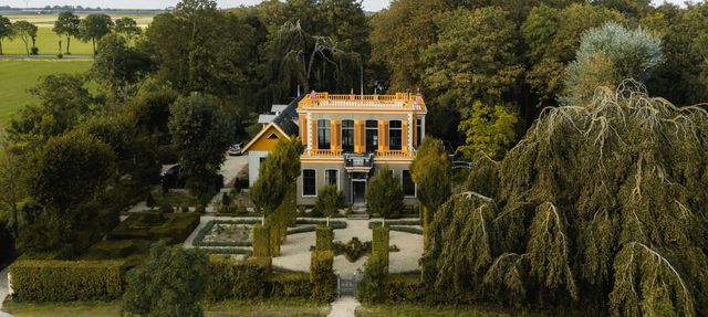 Je ziet een landhuis met parktuin