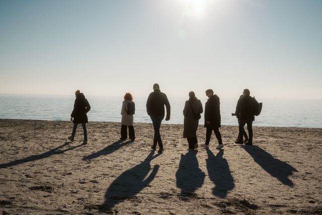 Een groep mensen loopt over het strand met op de achtergrond de zee en een laaghangende zon.