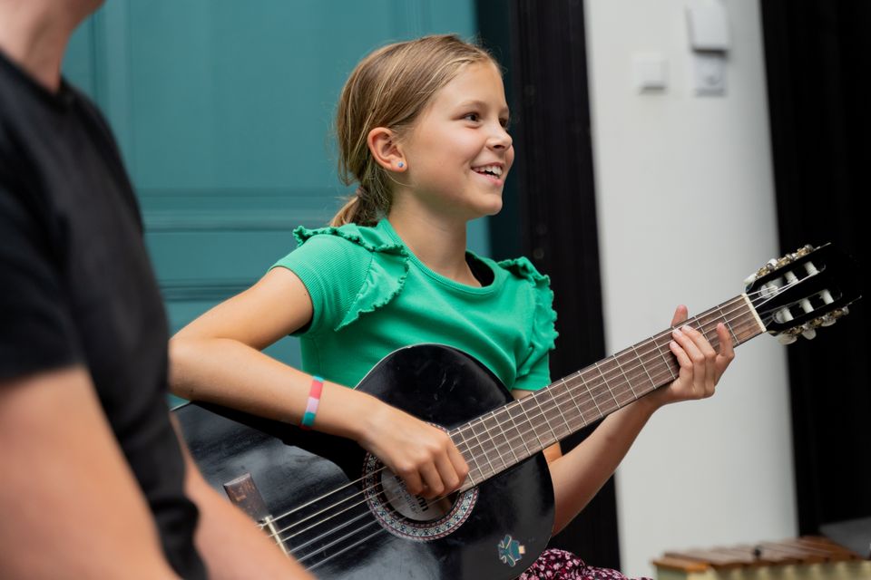 Muziekschool Muziekhuis in Oudewater, Groene Hart, meisje dat gitaarles volgt en akoestische gitaar speelt tijdens muziekles binnen de culturele ontmoetingsplek.