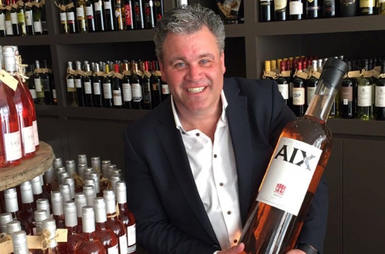 Eigenaar met grote fles rosé en op de achtergrond schappen met wijnflessen.