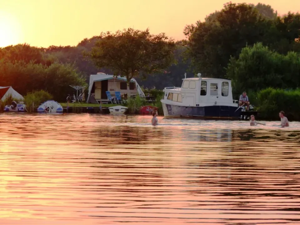 Boerderijcamping Poelzicht in Heeg vanaf het water met op de voorgrond verschillende mensen die in en om het water recreëren.