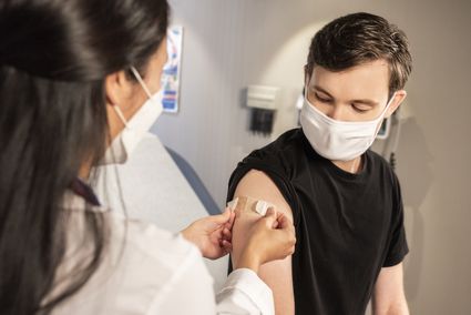 A nurse administers a vaccination to a patient. They are both wearing facemasks.