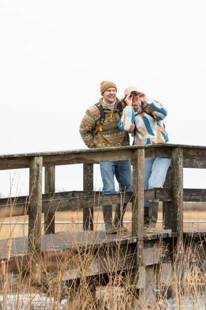 Twee mensen staan in winterkleding op een brug en één van hen kijkt door een verrekijker in de verte.