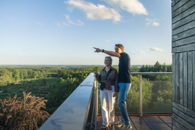 Man en vrouw staan op een uitkijktoren met boomtoppen op de achtergrond