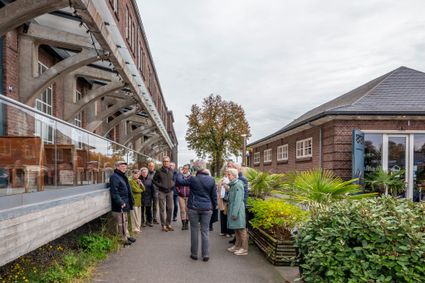 Groep mensen luistert naar het verhaal van de stadsgids voor het historische hoofdgebouw van de Leerfabriek.
