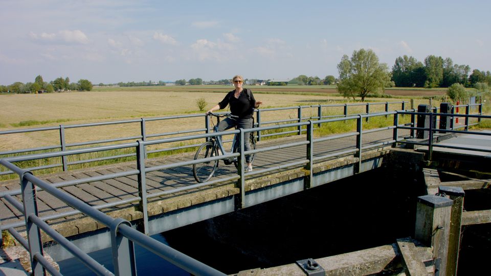 Een vrouw staat bovenop een houten sluis met een fiets.