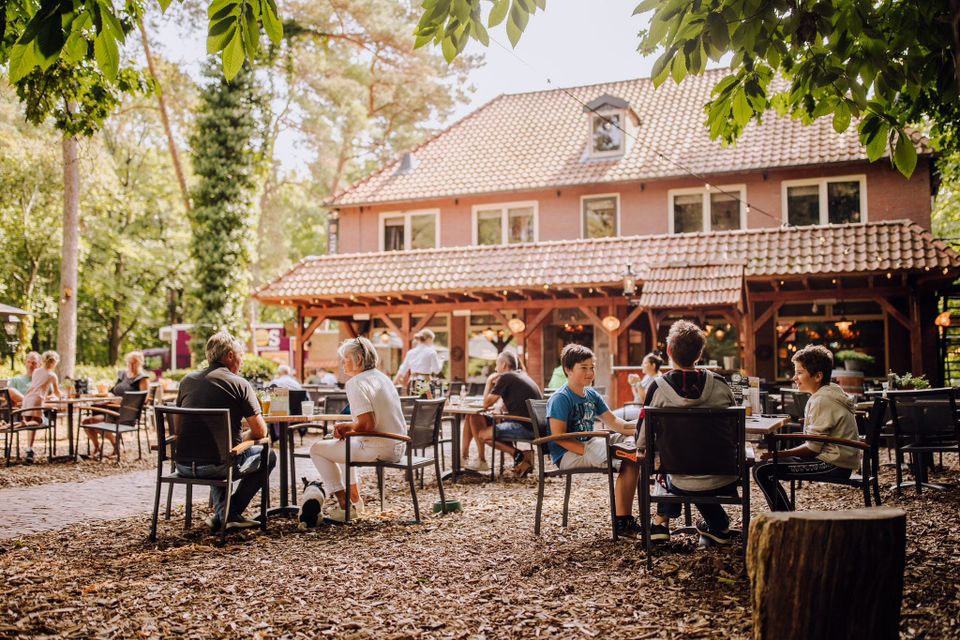 Terras in bosrijke omgeving met het hotel-restaurant op de achtergrond.