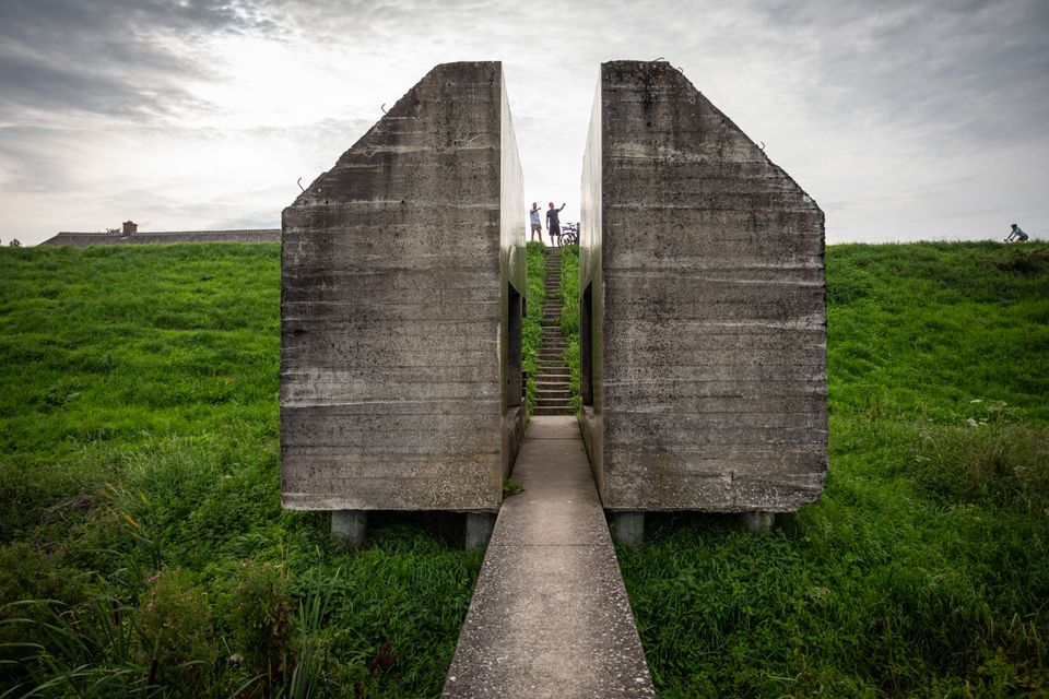 Twee personen zijn te zien in door een doorkijkje door een doorgezaagde bunker. Ze wijzen naar de bunker.