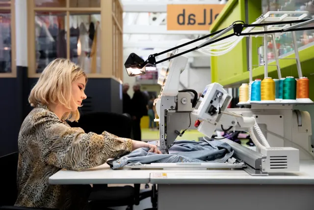 Een vrouw die achter een naaimachine in TexTielmuseum Tilburg.