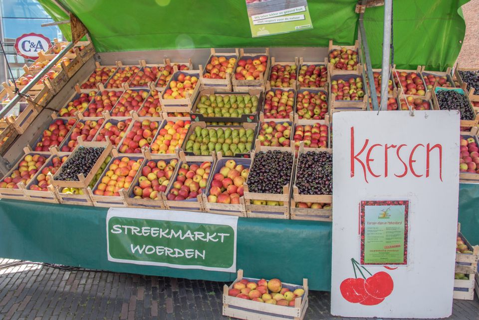 Marktkraam Streekmarkt Woerden in Woerden, Groene Hart, houten kisten vol kersen, appels en peren onder groene luifel met bord ‘Kersen’, verse streekproducten op de wekelijkse boerenmarkt.
