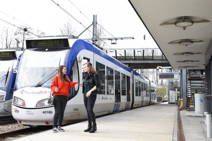 Twee mensen staan op het perron voor op de trein te wachten die eraan komt.