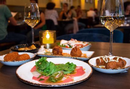 Een tafel gedekt met twee gevulde wijnglazen en borden met eten