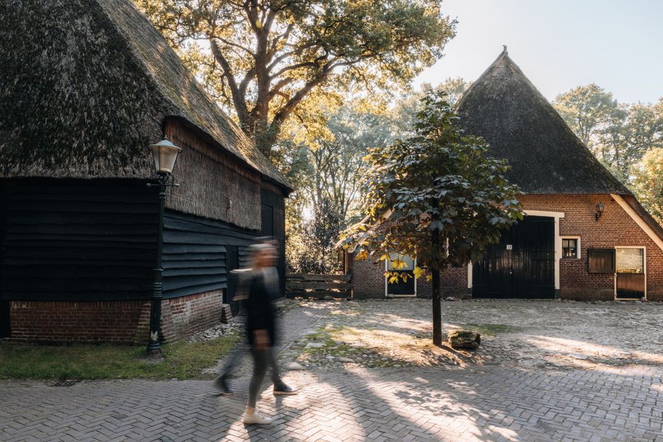Een man en een vrouw wandelen langs een authentieke Saksische boerderij in een Drents brinkdorpje.
