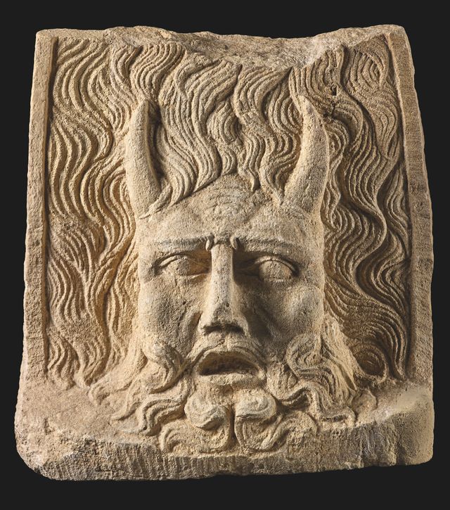 Stenen plaquette met een gehoornde god, met rivierstromen om zijn hoofd en een krullende baard.