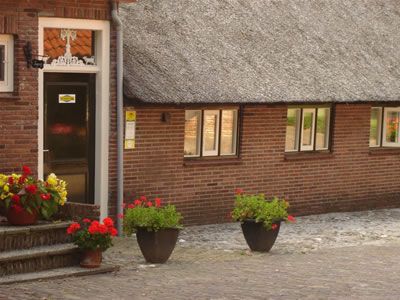 Rietgedekte boerderij van Zuivelmakerij De Staelenhoef met bloemen in potten bij de ingang.