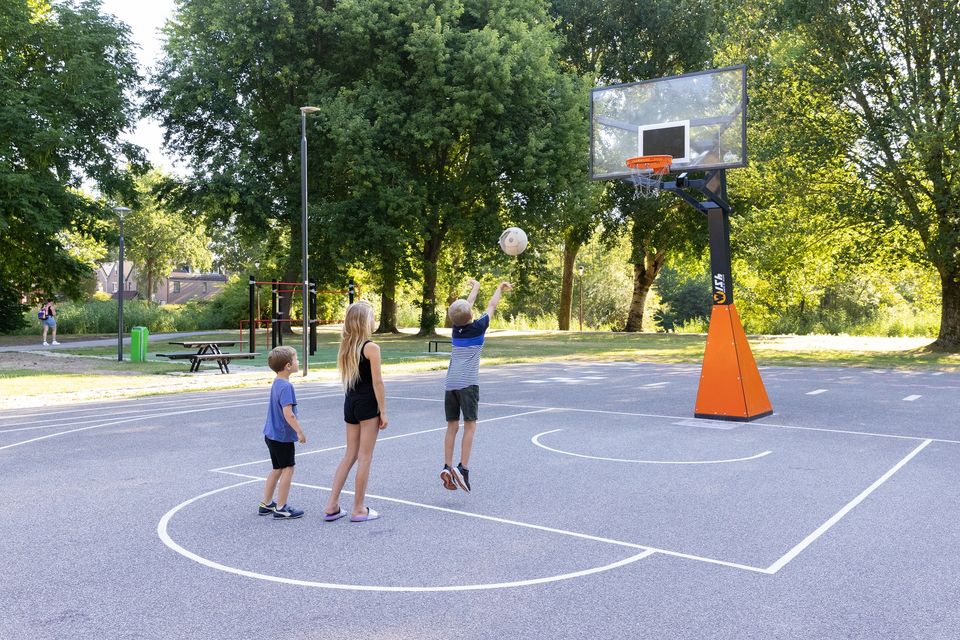 Drie kinderen spelen op het basketbalveld in park Kokkebogaard