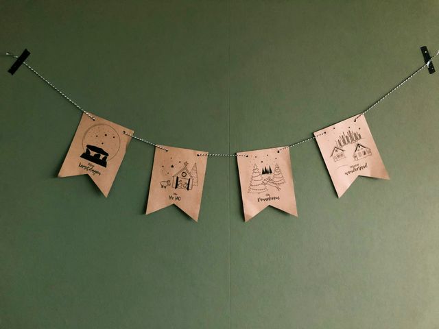 Een foto van een zelfgemaakte kerstslinger met Drentse plaatjes, tegen een groene muur.