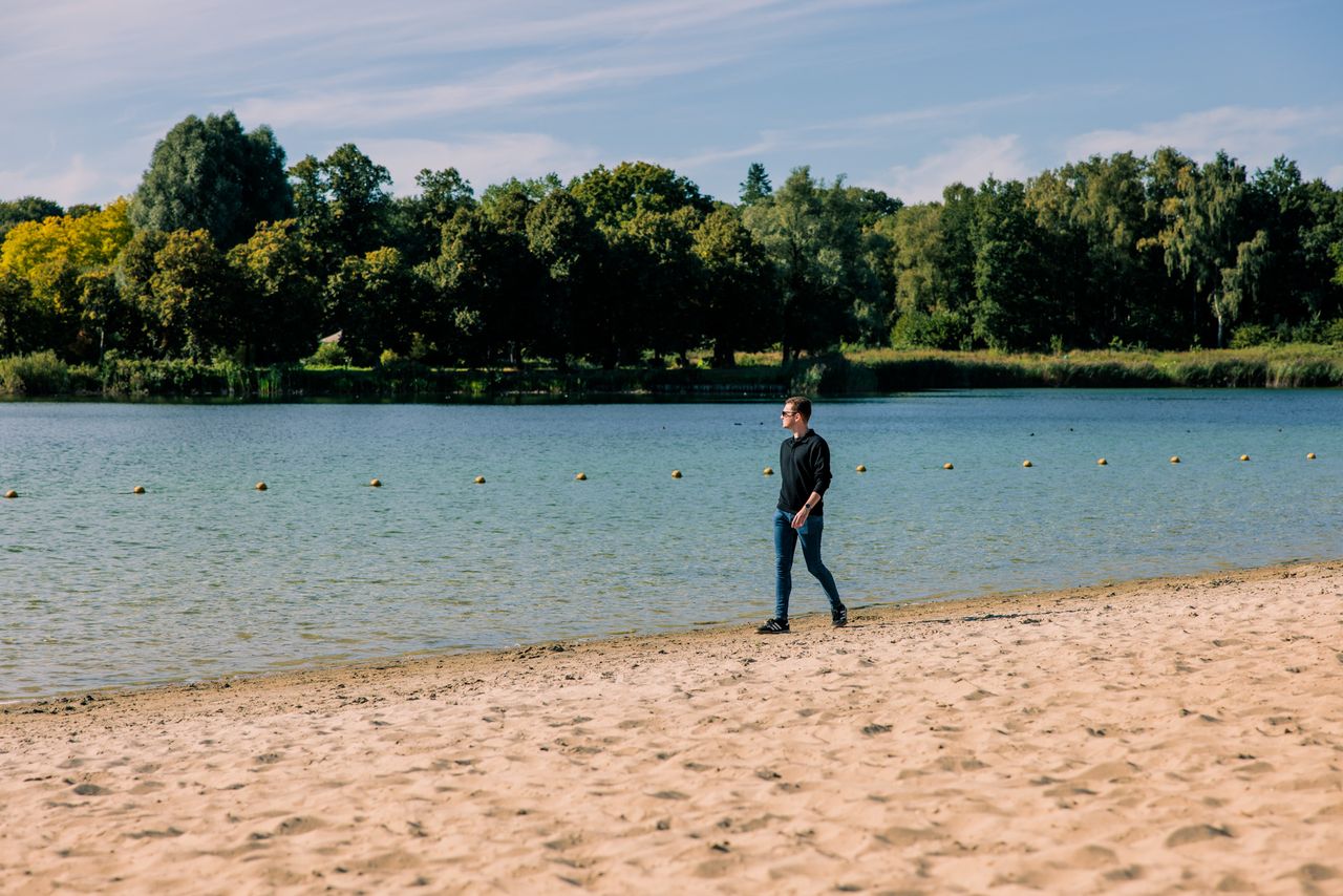 Jonge man loopt langs de kant van het water op een zandstrand.