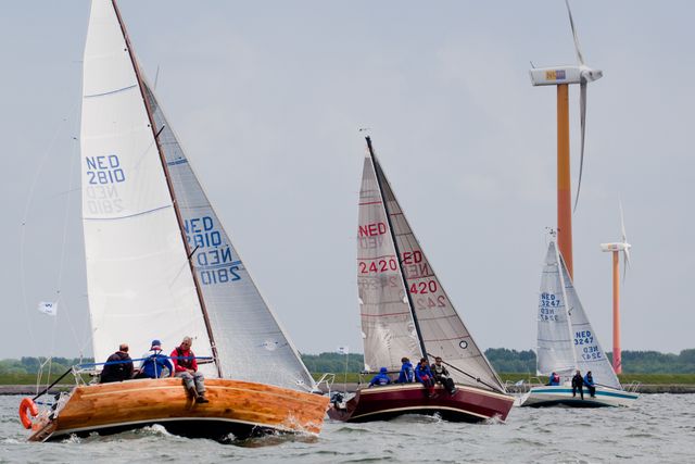 Zeilers varen op water met golven en een windmolen in het landschap tijdens Almere Regatta in Flevoland