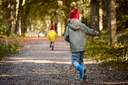 Twee kindjes met kaboutermutsjes op rennend over een bospad in Oudemirdum in de herfst.