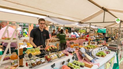Boerenmarkt Streekmarkt Woerden, Groene Hart, provincie Utrecht, kraam met streekproducten zoals sap, kaas, groente en huisgemaakte lekkernijen onder een markttent met winkelend publiek op het plein.