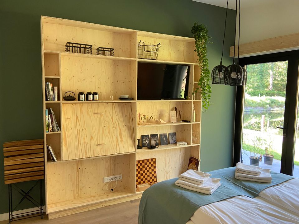 Slaapkamer met licht houten TV-kast, met open vakken tegen een groene muur, met uitzicht op de vijver.
